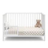 white crib in toddler bed conversion with one guardrail