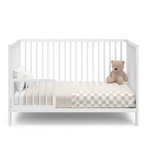 white crib in toddler bed conversion with one guardrail