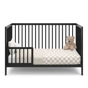 Black crib in toddler bed conversion with one guardrail