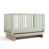 Baby crib in two-tone sage and natural wood colorway, at an angled view (Sage with Driftwood) 