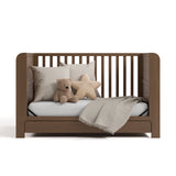 Read-with-Me crib hazelnut daybed conversion with pillows, stuff toys, and a blanket