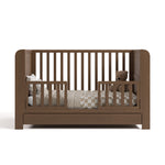 Read-with-Me crib hazelnut toddler bed conversion with pillows, bedding, and teddy bear