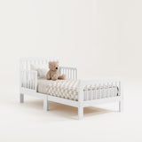 Angled view of a white toddler bed with bedding and teddy bear