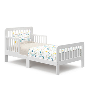 Angled view of a white toddler bed with bedding