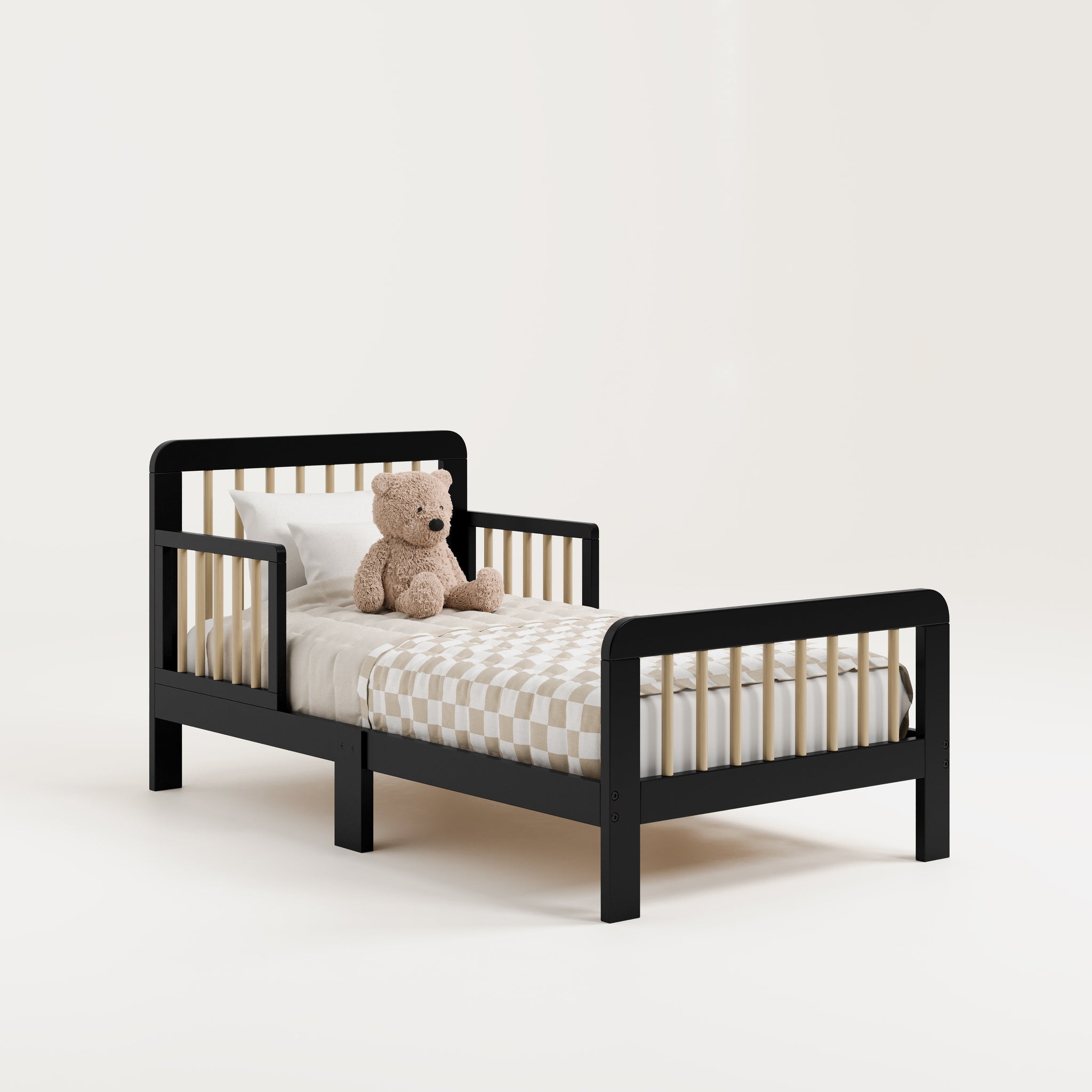 Angled view of a black toddler bed with driftwood finish with bedding and teddy bear