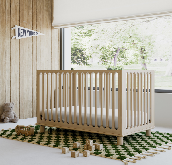 Natural wood baby crib on checkered rug with various baby toys on the floor