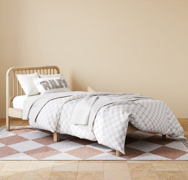 Natural wood bed on copper colored diamond checkered rug, and bed has pillow that says RILEY on it