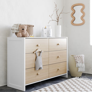 Two-tone white and natural wood six-drawer double dresser in room setting, surrounded by various decorative objects and bedroom accessories